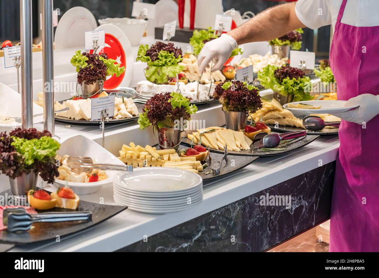 Hotel open buffet breakfast selection.. Service staff putting some cheese to plate during service. Delicious type of cheese in the counter. Stock Photo