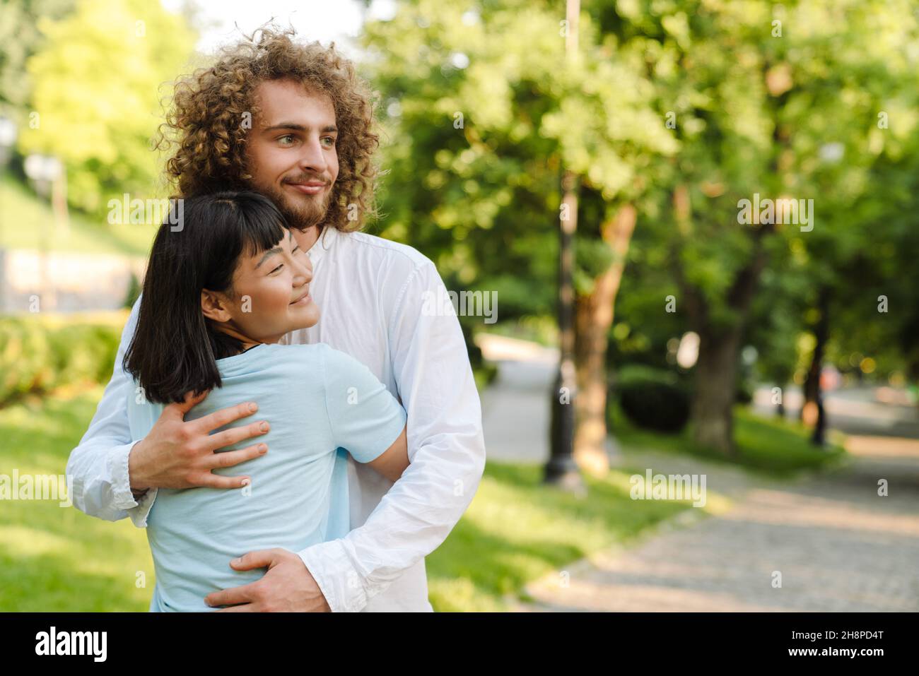 Happy young multiethnic couple cuddling embracing together in the green park Stock Photo
