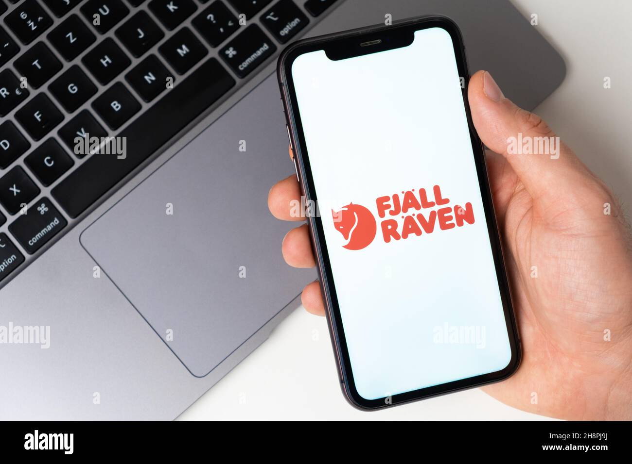 Fjallraven app logo on the iPhone screen for online shopping with a laptop on the background. November 2021, San Francisco, USA Stock Photo