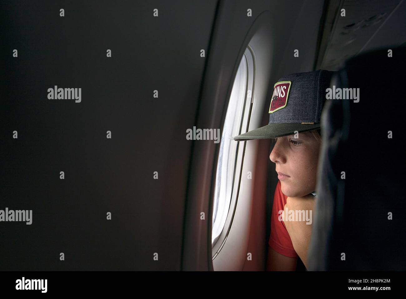 Boy with cap looking out airplane window Stock Photo