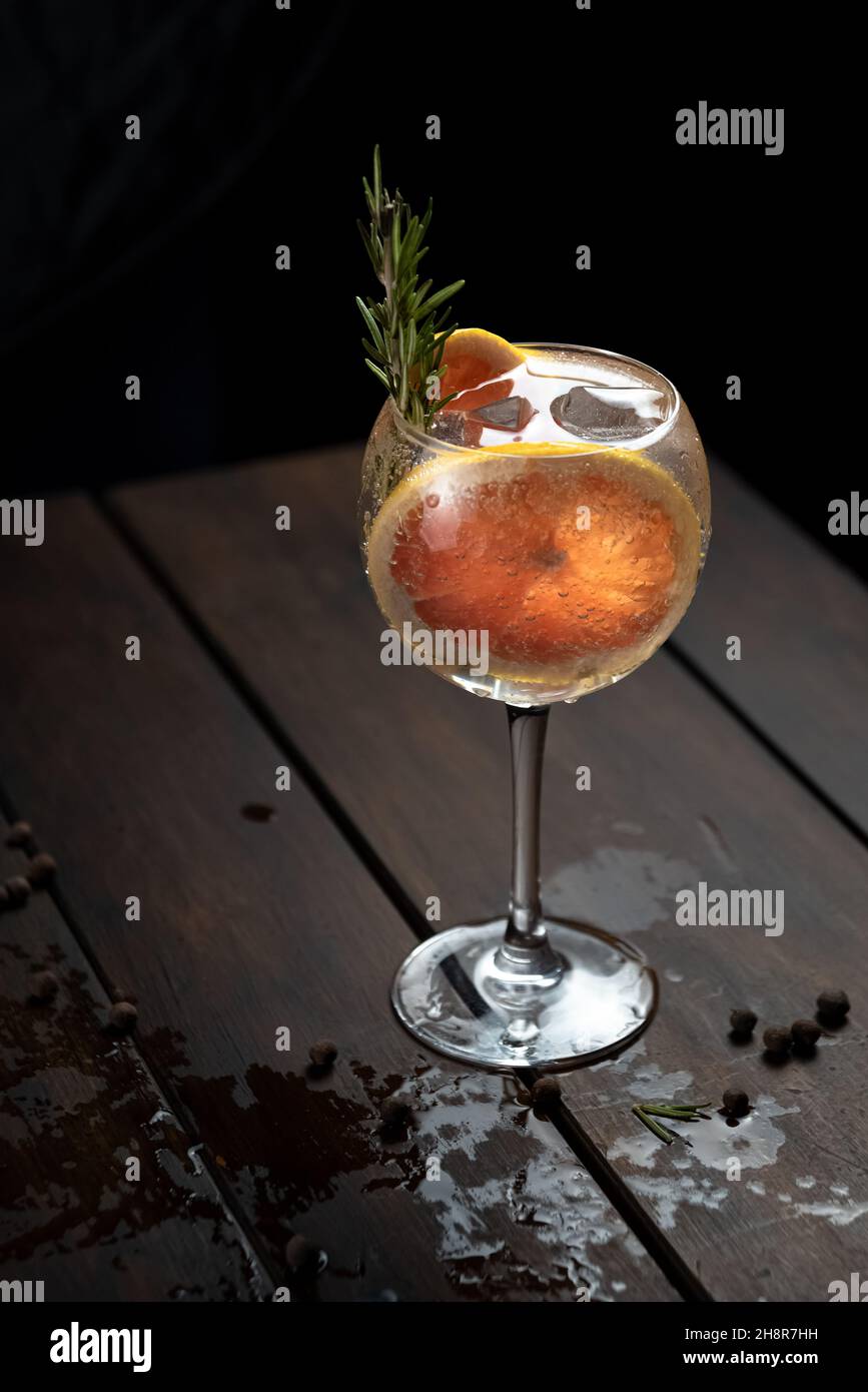 Bebida alcohólica (trago de gin and tonic) con rodaja de pomelo y hielo en rústica mesa de madera mojada. Stock Photo
