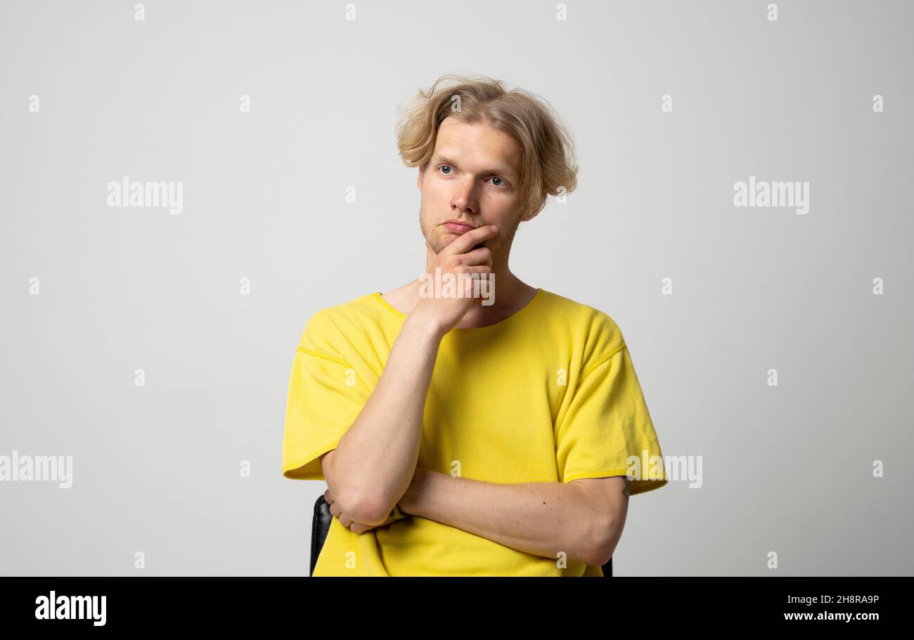 Portrait of thoughtful young man who looks away and touching his chin and weighs the pluses and minuses of the offer isolated on white background with Stock Photo