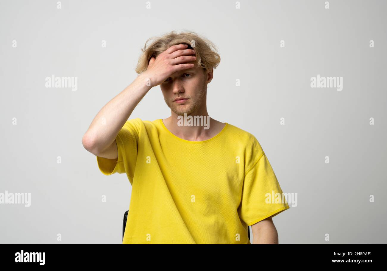 Young man doing facepalm gesture. Portrait of ashamed abashed man in yellow t-shirt covering his face with hand on a white background. Copy space for Stock Photo
