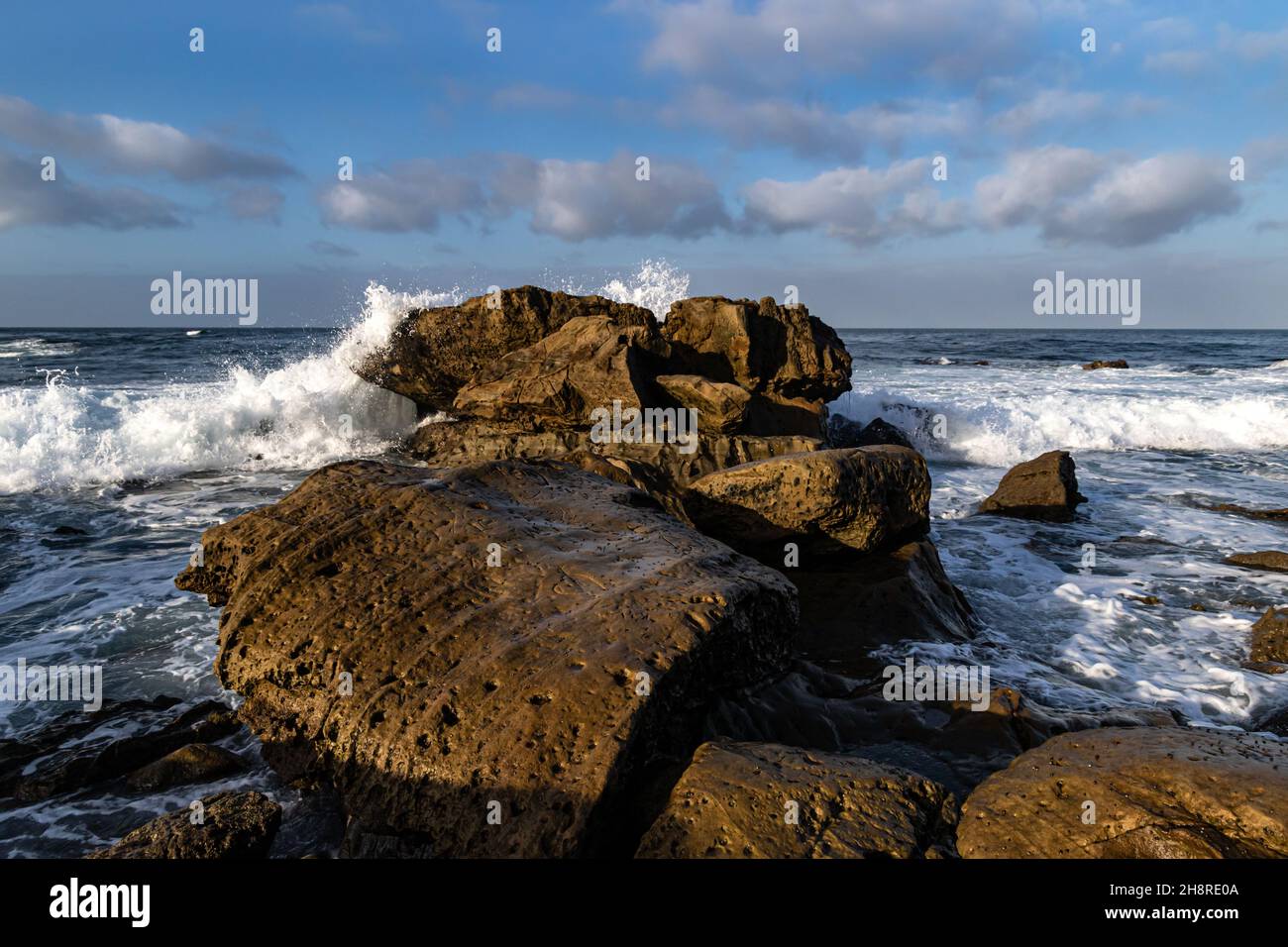 Wave crashing onto rocks, Southern California shoreline at Laguna Niguel. Blue sky and clouds in the distance. Stock Photo