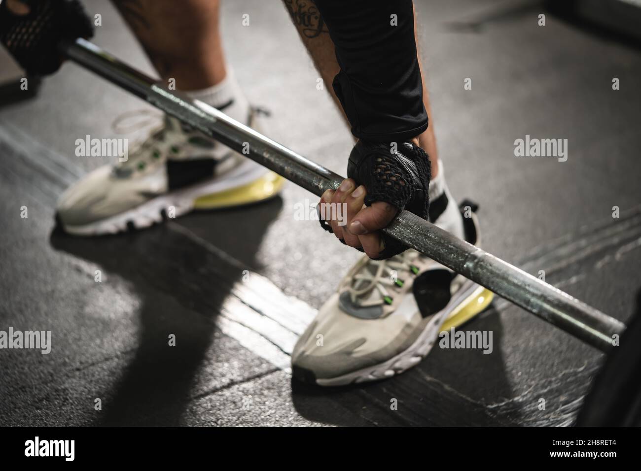 Close up on hand of unknown caucasian man holding barbell weight grip at gym lifting weights in training wearing dark black gloves low section copy sp Stock Photo