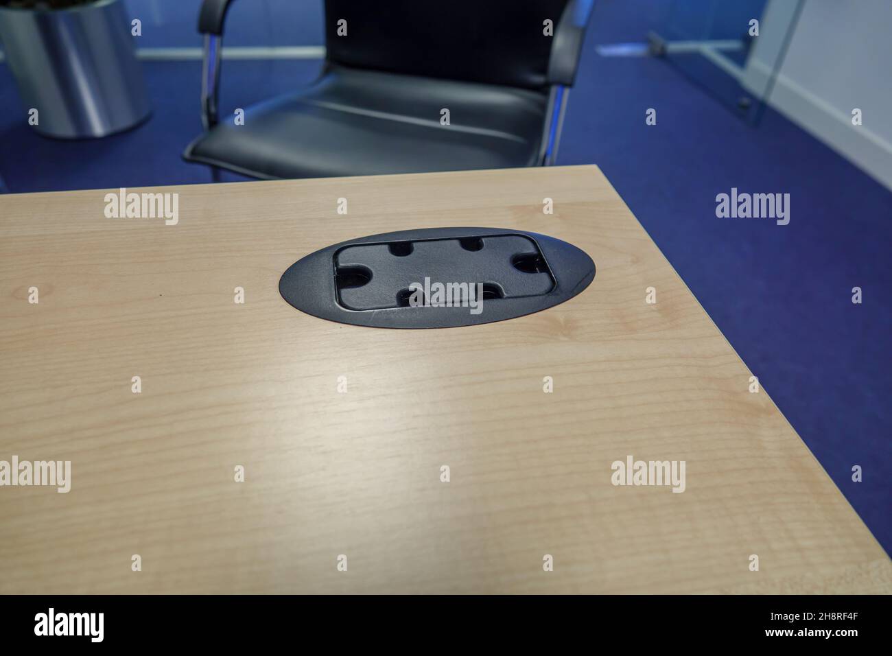 black plastic office desk cable tidy in a light oak coloured desk with black and chrome office