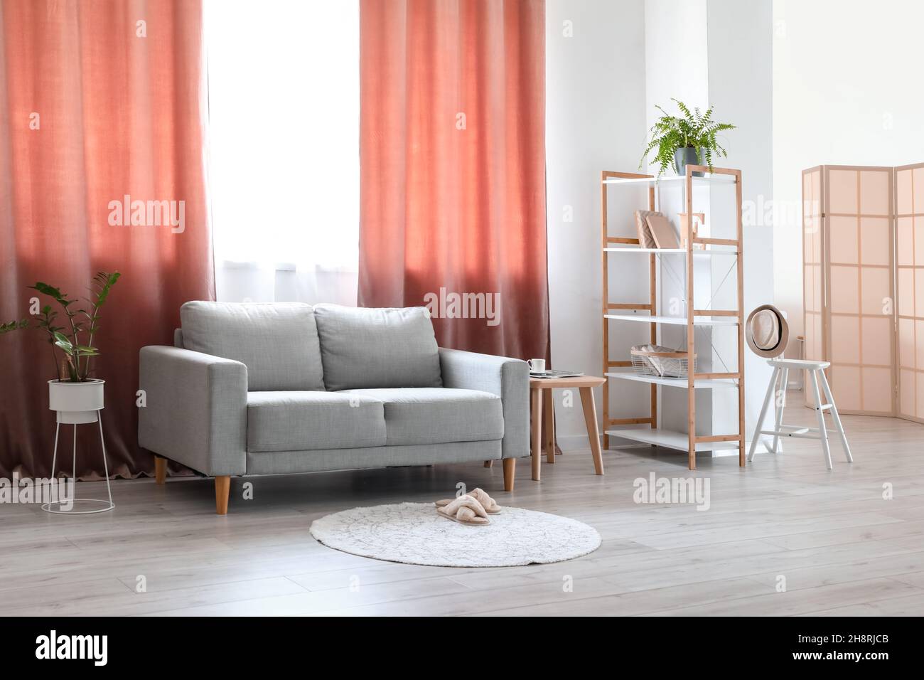 Interior of light living room with grey sofa, shelving unit and red  curtains Stock Photo - Alamy, image size:1300x956