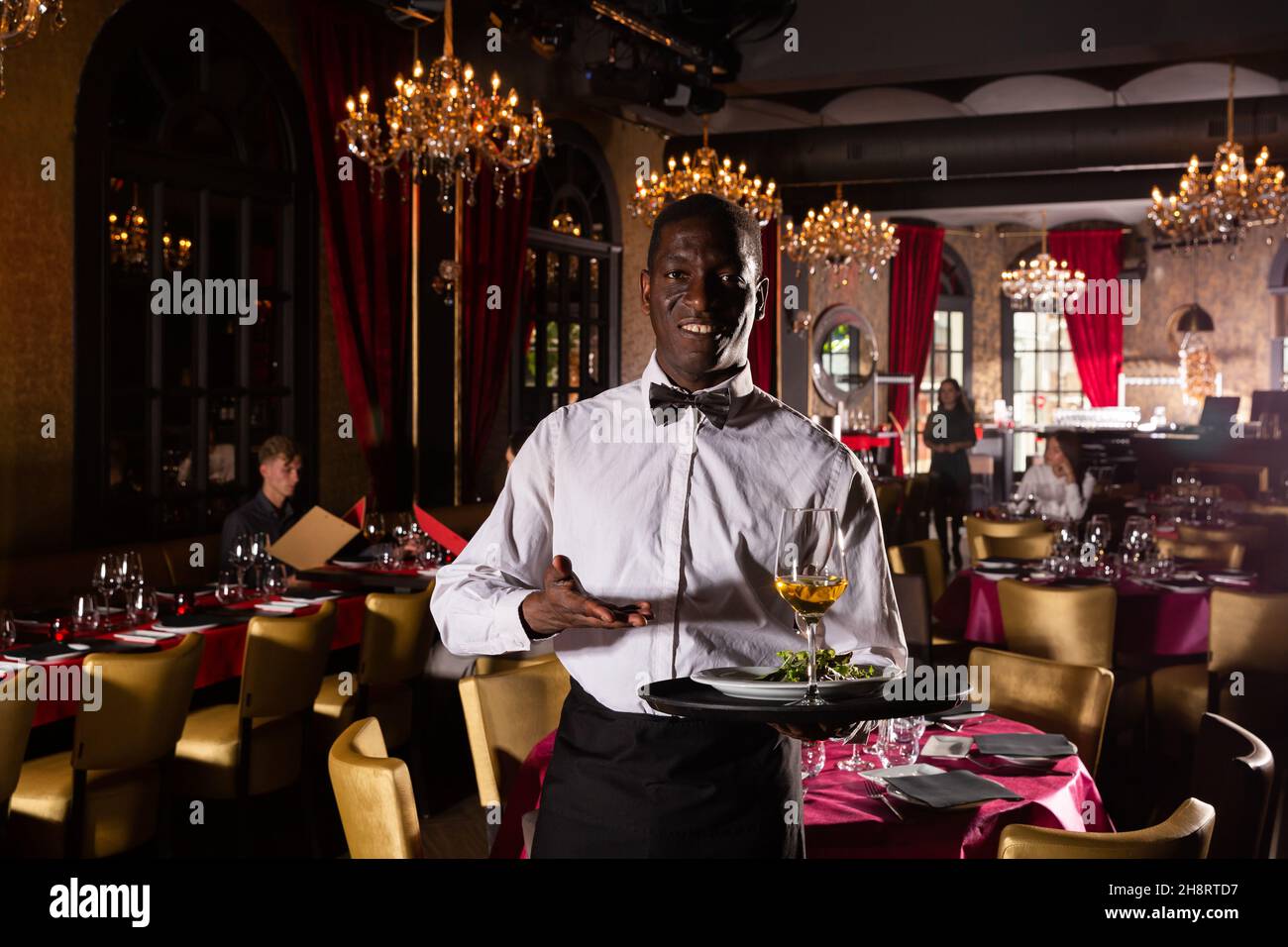 Hospitable africanamerican waiter standing with serving tray meeting