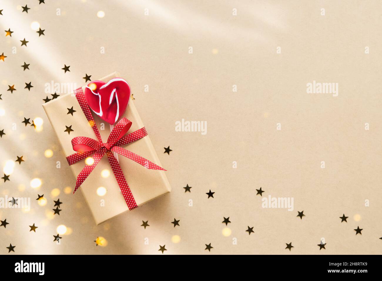 Christmas gift box decorated with red ribbon and heart-shaped lollipop on a kraft paper background. Top view, copy space for text Stock Photo