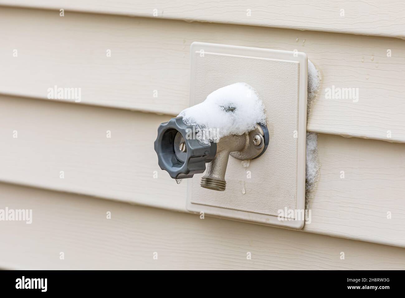 Outdoor water spigot covered in snow during winter. Home repair, maintenance and weatherproofing concept Stock Photo