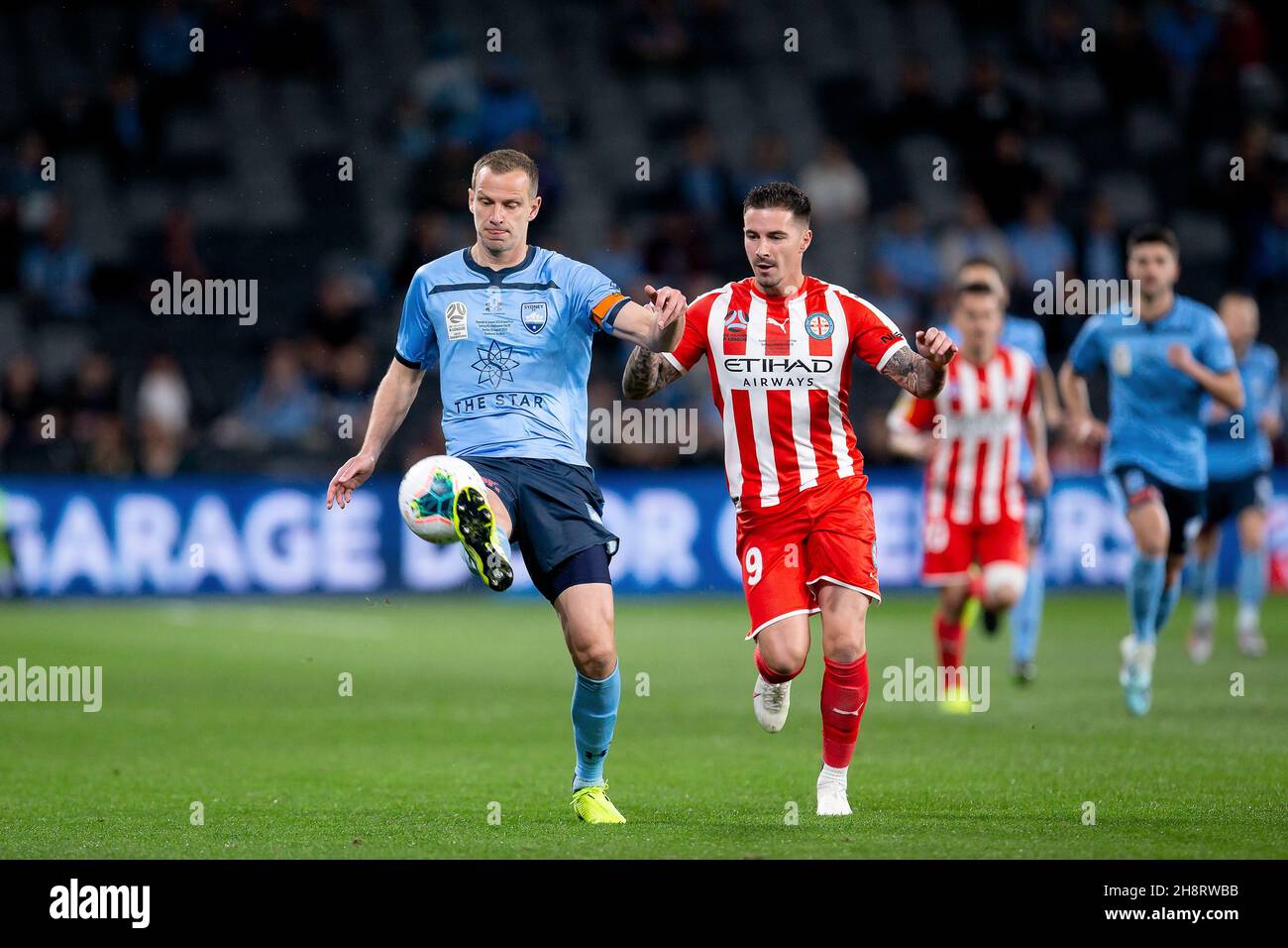 Sydney FC defender Alex Wilkinson (4) clears the ball under pressure from Melbourne City forward Jamie Maclaren (9) (Photo by Damian Briggs/ Speed Media) Stock Photo