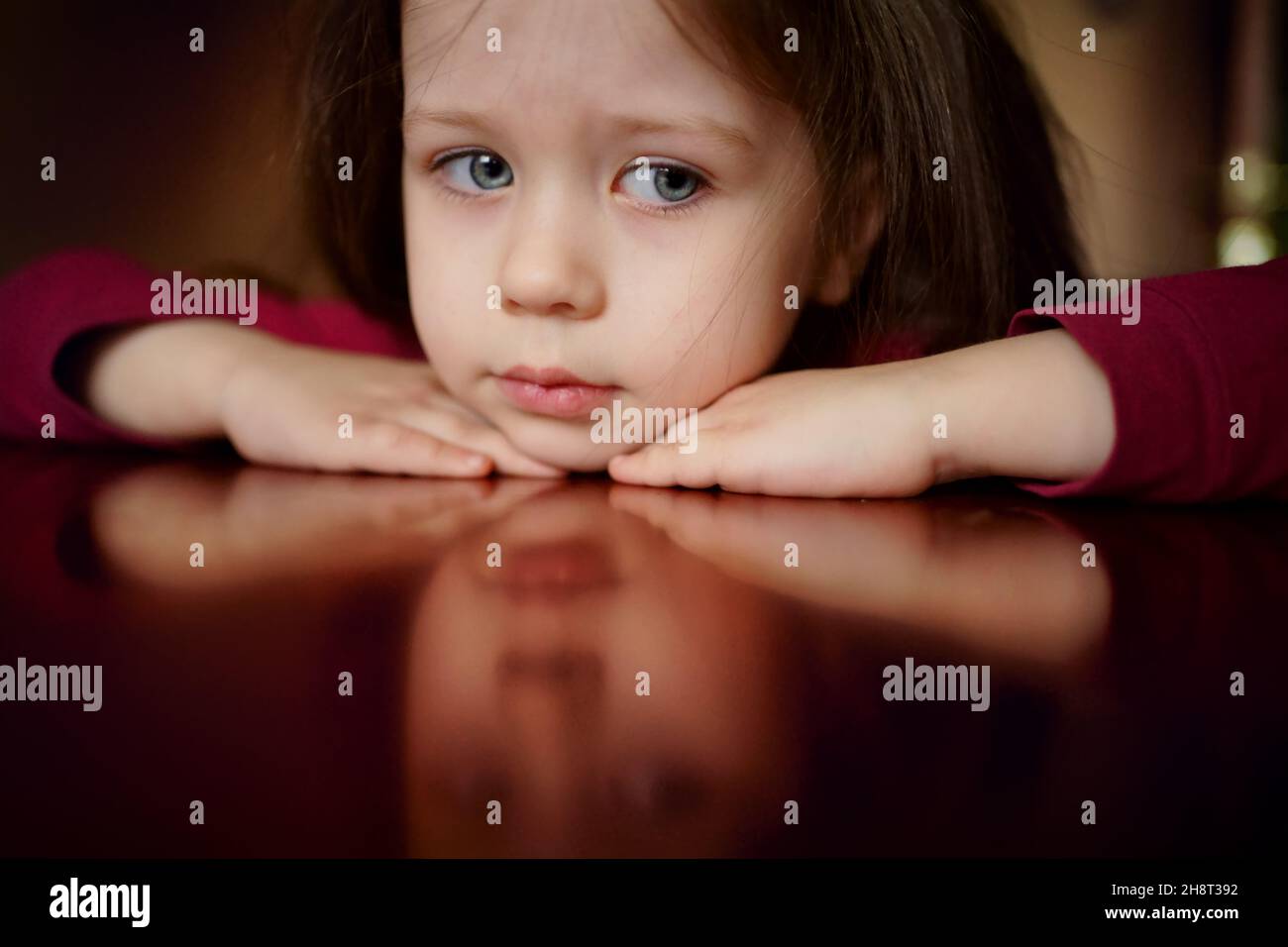 Sad head of a little girl lies on the table, thinks, upset, offended, face reflection Stock Photo