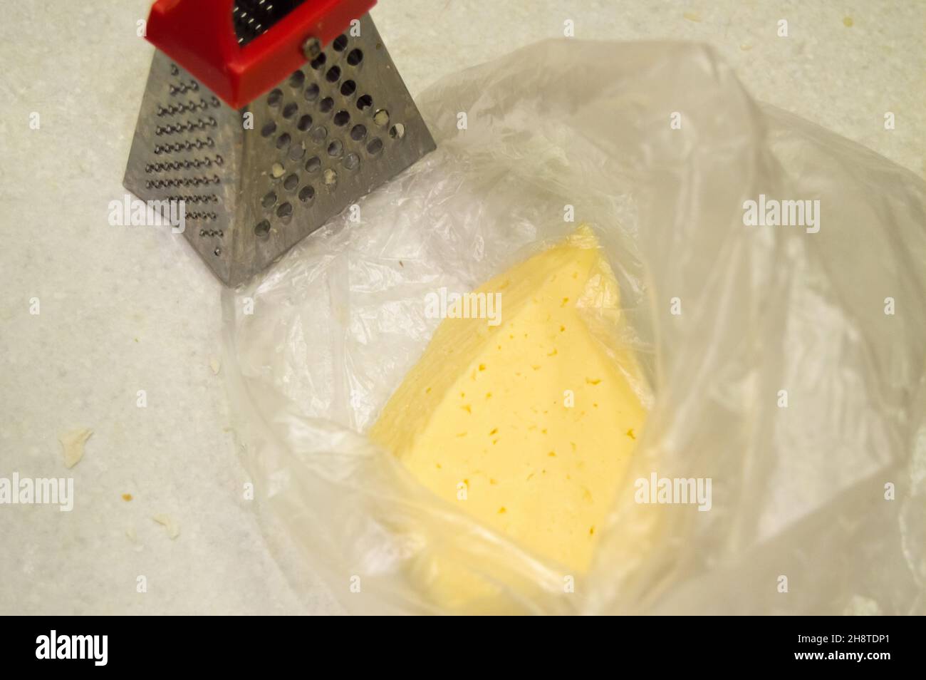 https://c8.alamy.com/comp/2H8TDP1/a-piece-of-cheese-in-a-plastic-bag-next-to-a-small-metal-grater-non-ecological-packaging-2H8TDP1.jpg