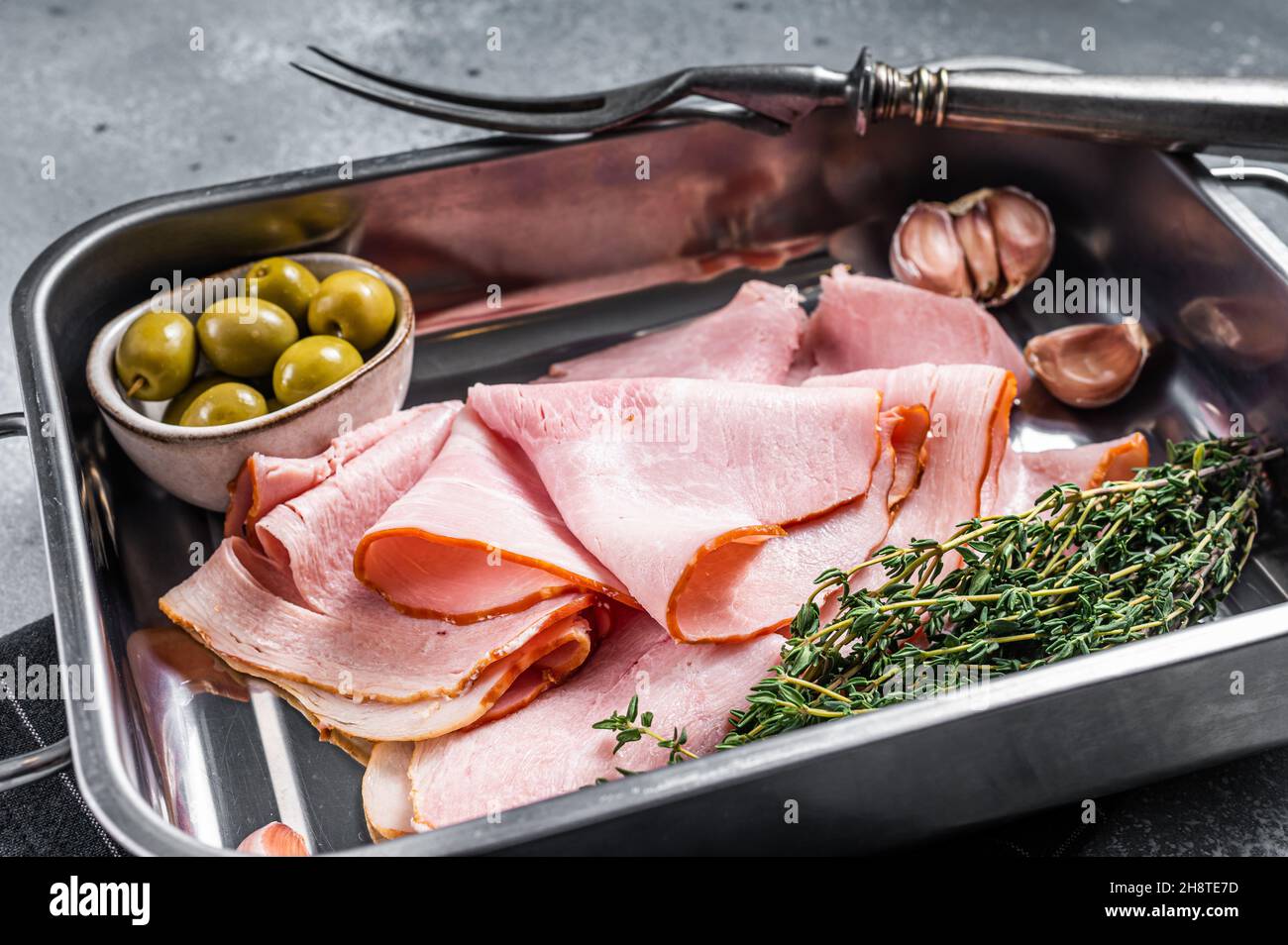 Ham slices in kitchen tray with herb and olives, Italian Prosciutto cotto. Gray background. Top