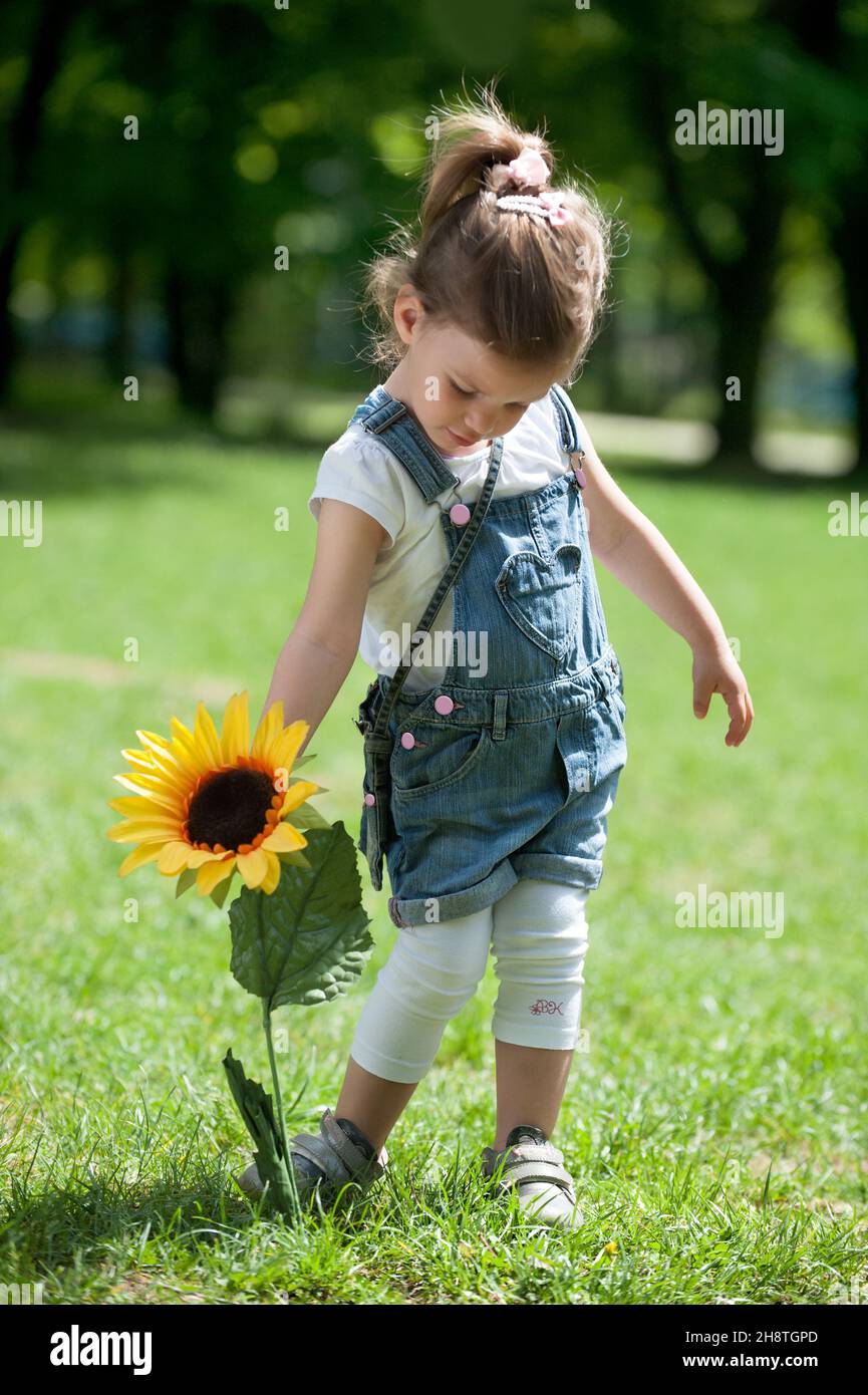 Cute little girl with a sunflower in the green spring grass Stock Photo ...