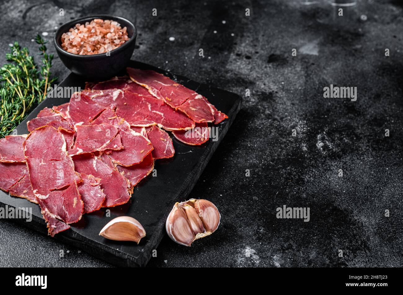 Sliced Pastrami roasted beef meat with herbs. Black background. Top view. Copy space Stock Photo