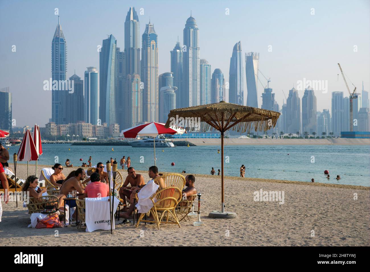 Relaxing on the beach at Koko Bay with a view towards the skyscrapers at Dubai Marina, The Palm, Dubai Stock Photo