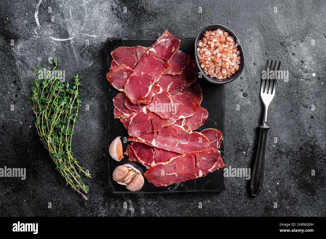 Sliced Pastrami roasted beef meat with herbs. Black background. Top view Stock Photo