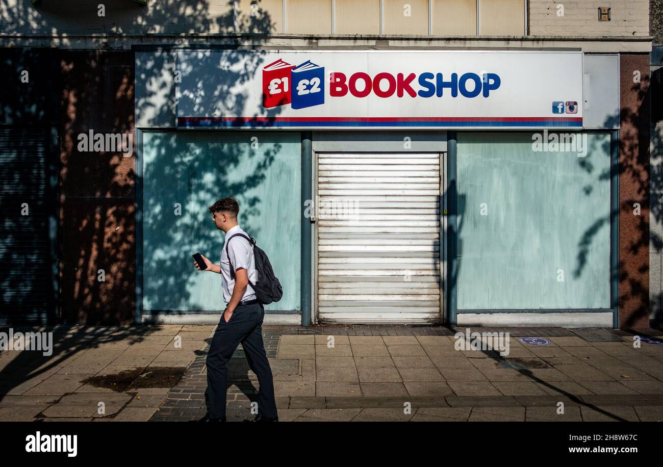 Man using his mobile, walking past a closed book shop in Rotherham Stock Photo