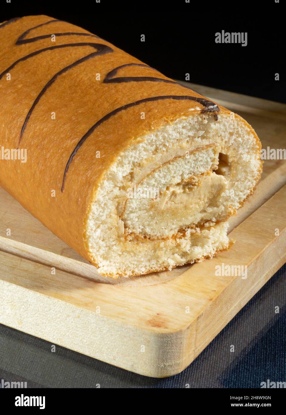 Sweet roll on a wooden board in the kitchen. Food products on a black background Stock Photo