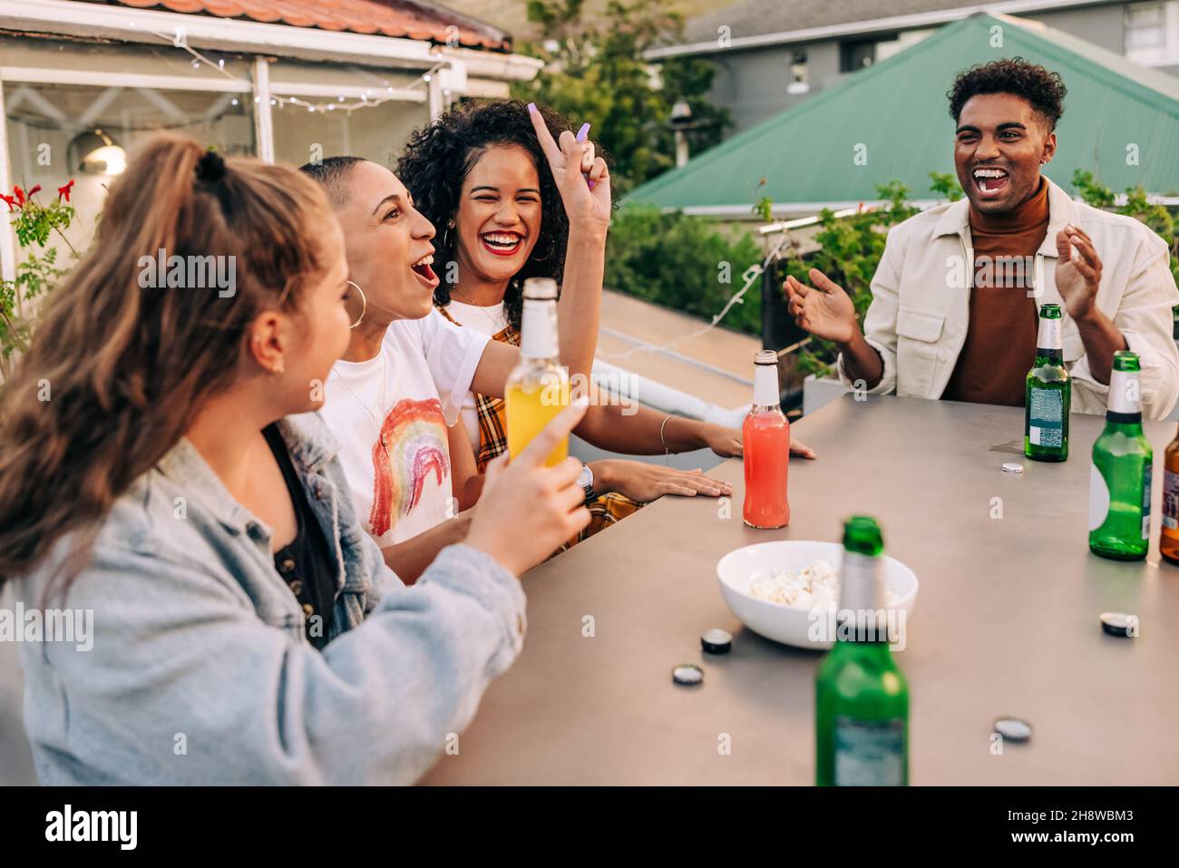 Having cold beers and a good time. Group of happy young people laughing together while hanging out on a rooftop. Cheerful friends enjoying alcoholic d Stock Photo