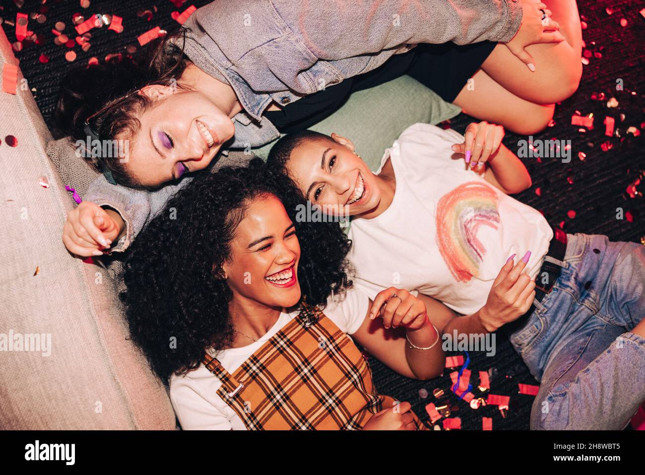 Overhead shot of happy female friends lying on the floor at a house party. Group of three young women laughing and having a good time. Cheerful young Stock Photo