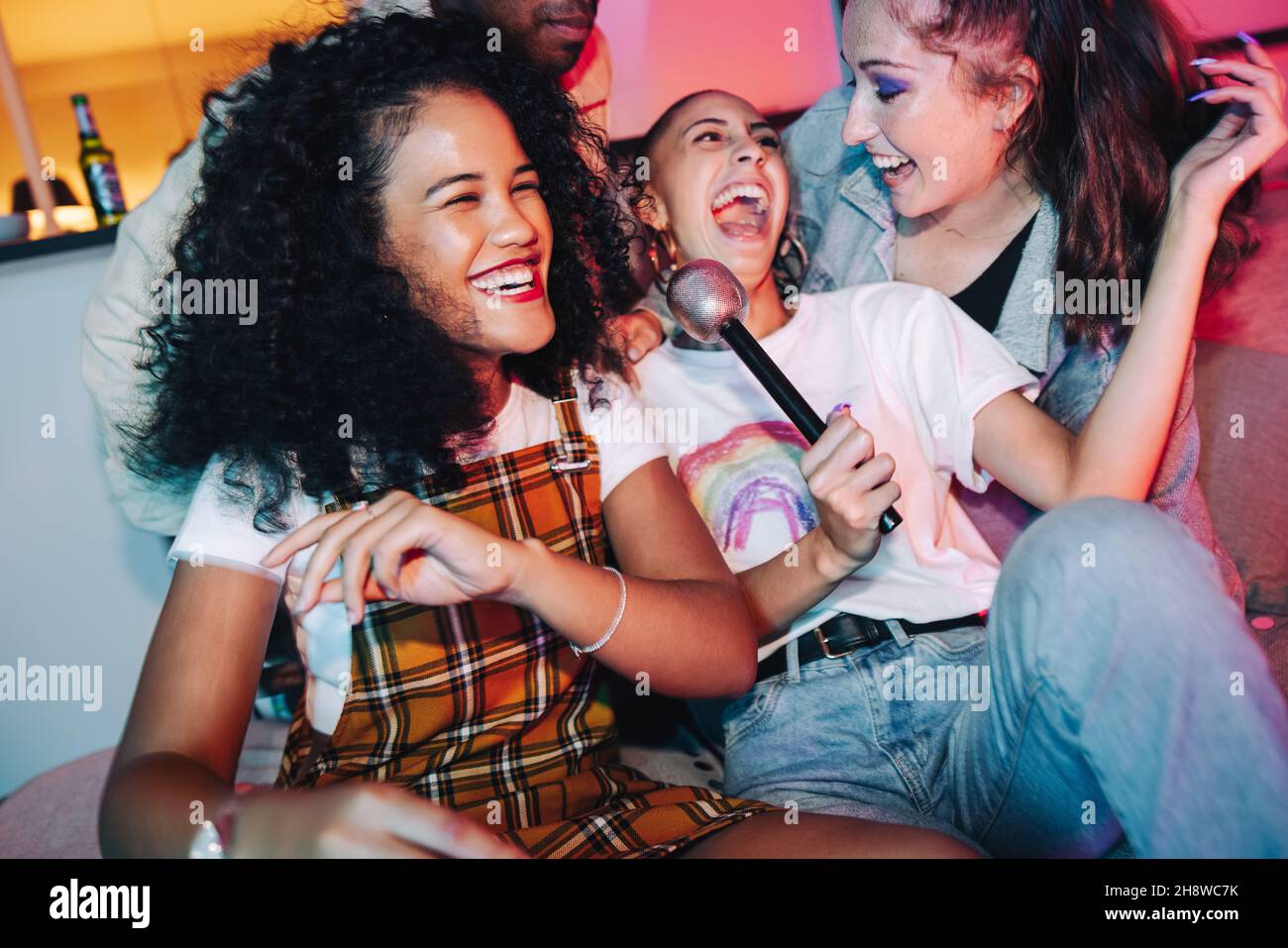 Karaoke happiness. Cheerful friends enjoying singing their favourite songs during karaoke night. Group of multicultural friends laughing and having a Stock Photo