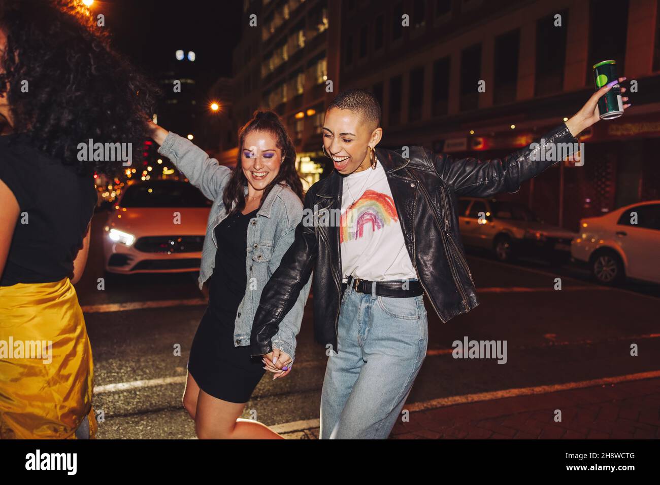 Dancing on a weekend night. Two cheerful female friends dancing happily while crossing a street in the city. Two vibrant young women laughing and havi Stock Photo