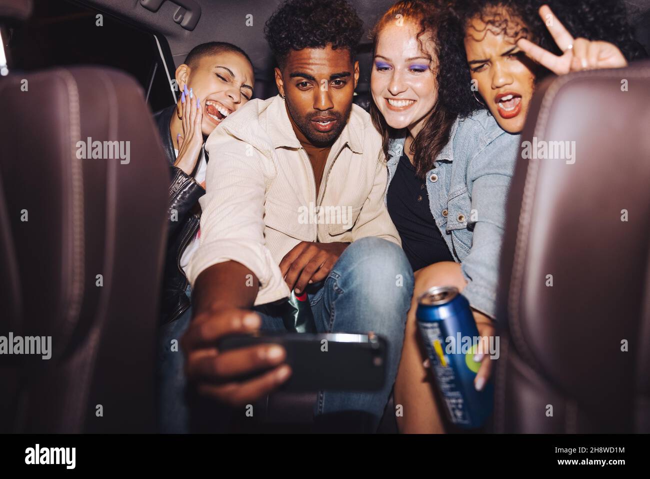 Diverse group of friends taking a selfie together inside a car. Group of young friends posing for a group photo in front of a camera phone. Carefree f Stock Photo