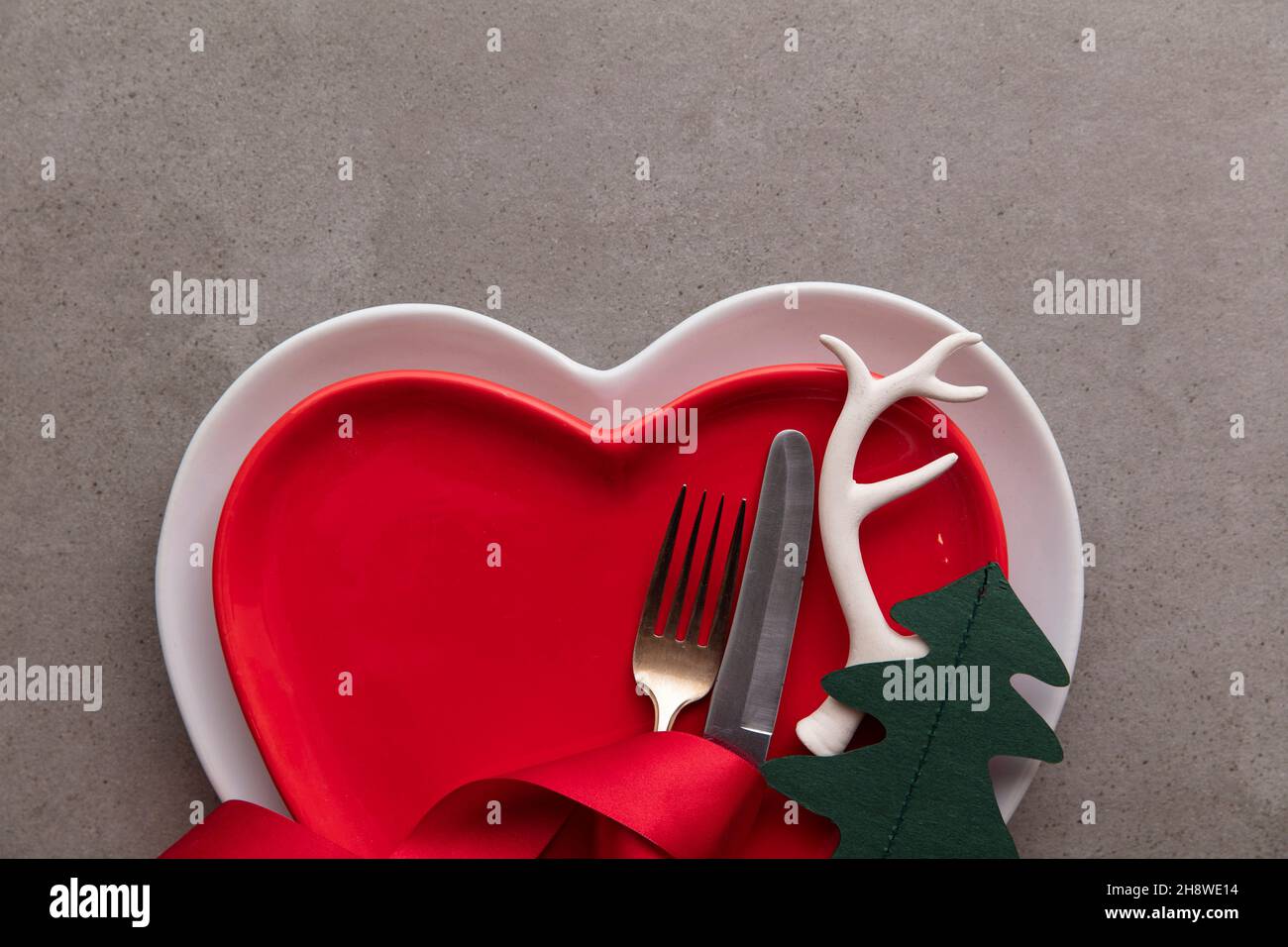 Festive Christmas meal background. Heart shaped plate with knife and fork and Christmas antler and tree decorations Stock Photo