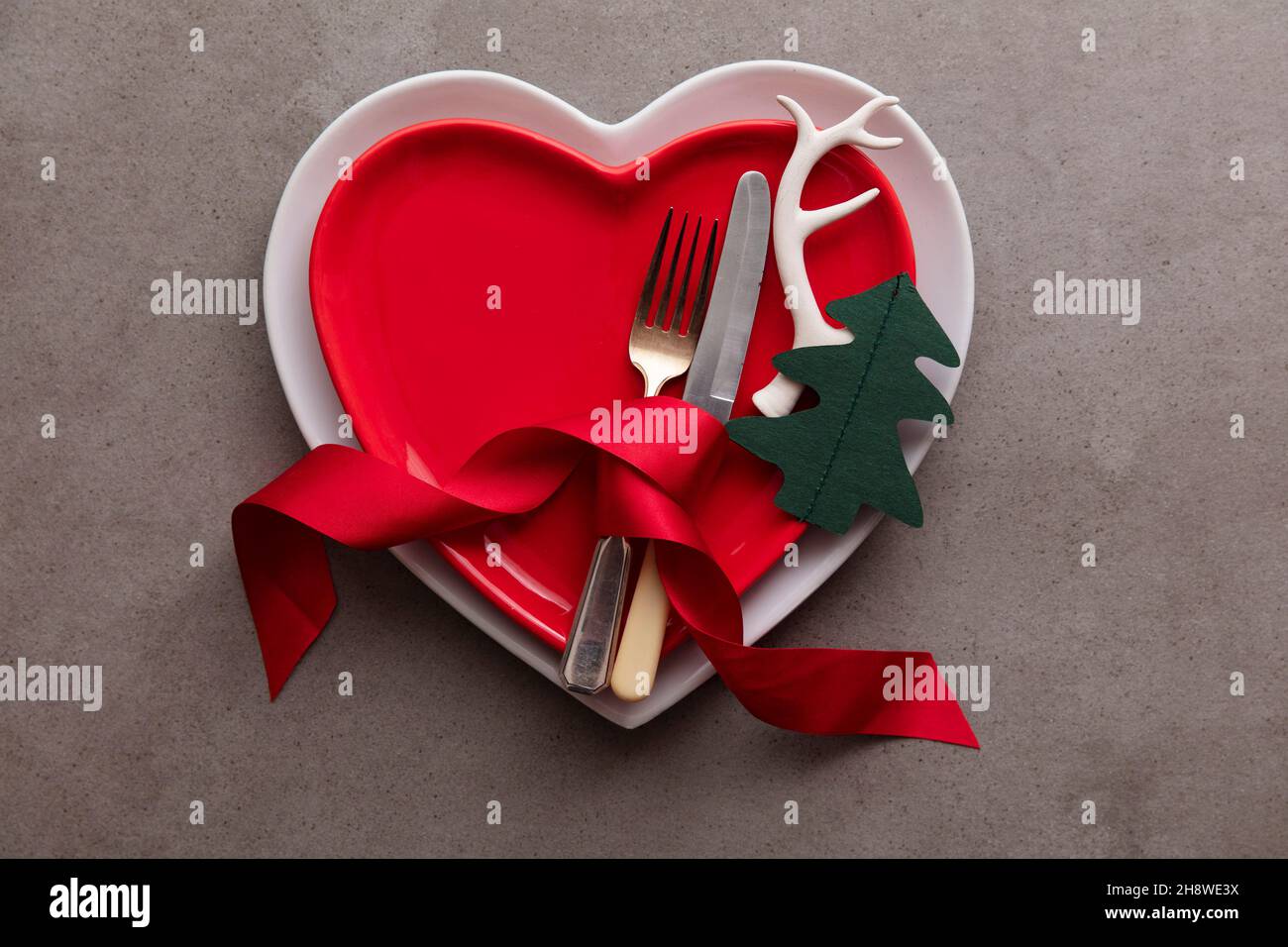 Festive Christmas meal background. Heart shaped plate with knife and fork and Christmas antler and tree decorations Stock Photo