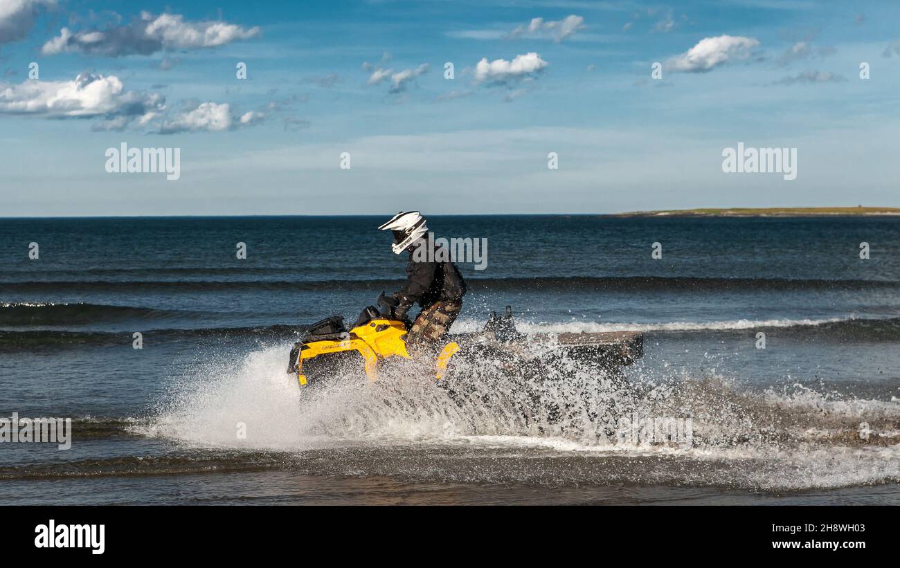 Russia, Kola Peninsula, June 20, 2013: An ATV rider rides splashing water along the shores of the Barents Sea. Motion blur, selective soft focus. Stock Photo
