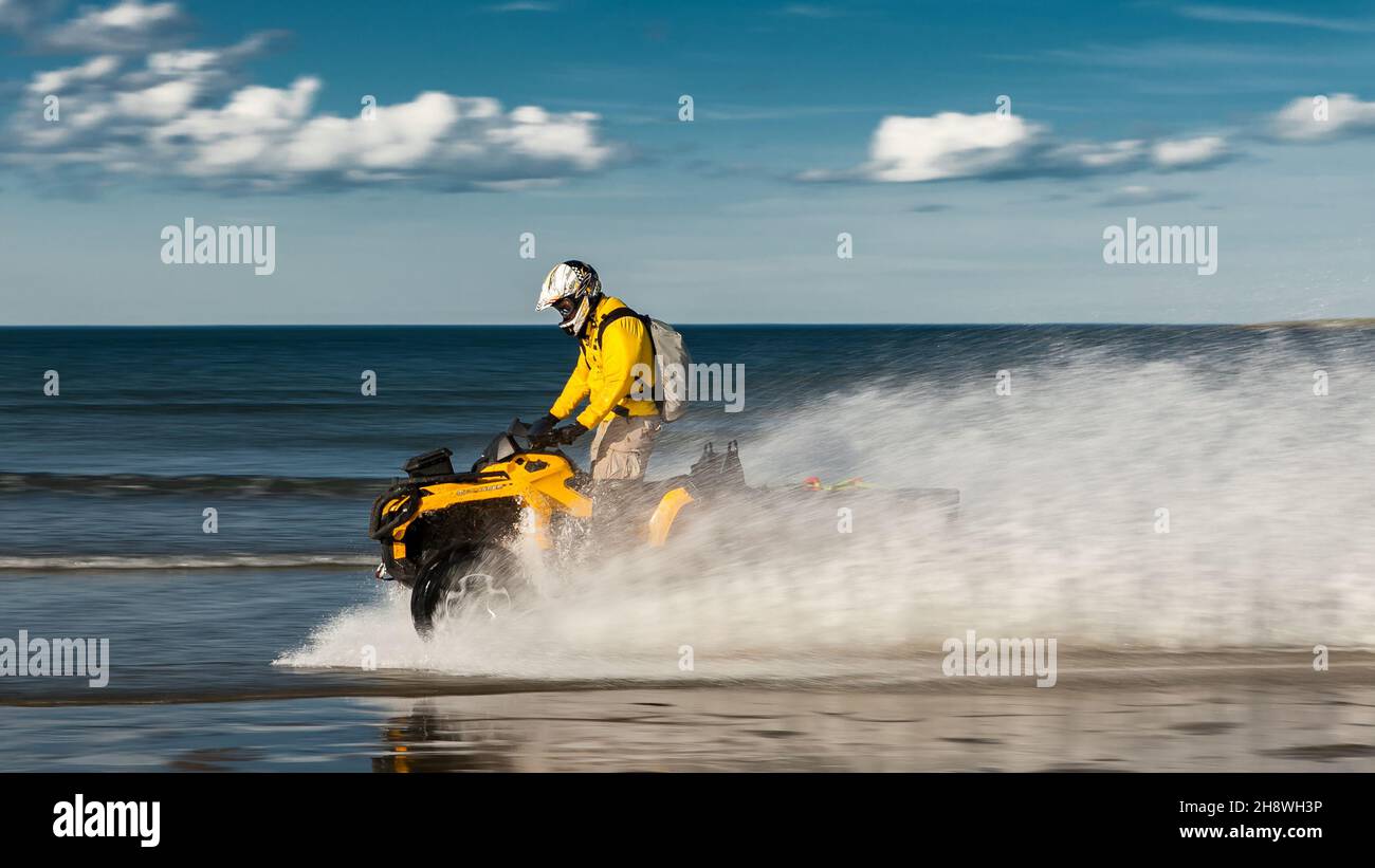 Russia, Kola Peninsula, June 20, 2013: An ATV rider rides splashing water along the shores of the Barents Sea. Motion blur, selective soft focus. Stock Photo