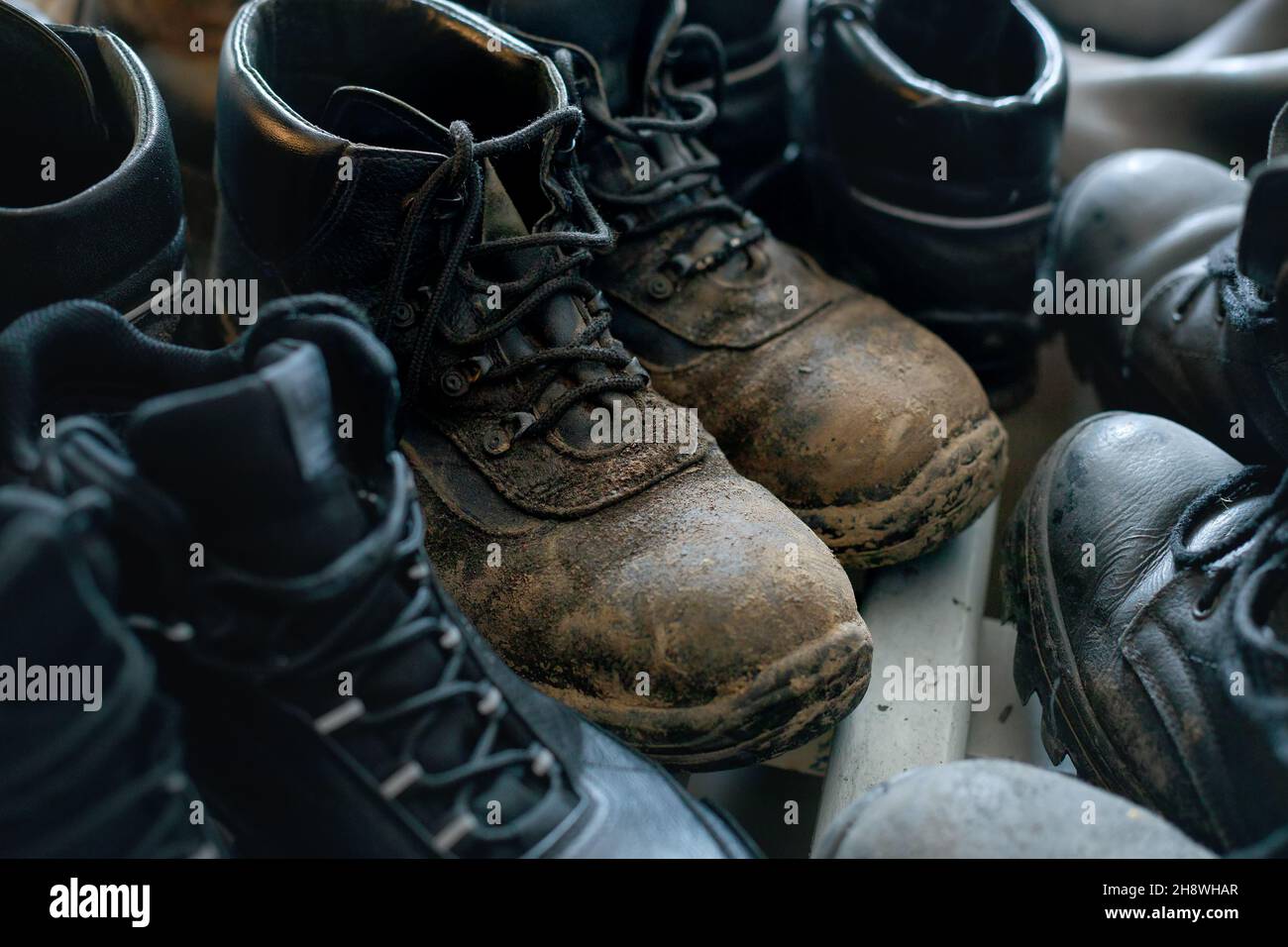 Many old work boots stand together. Old worn construction boots of workers. Background. Real scene. Shift shoes. Stock Photo