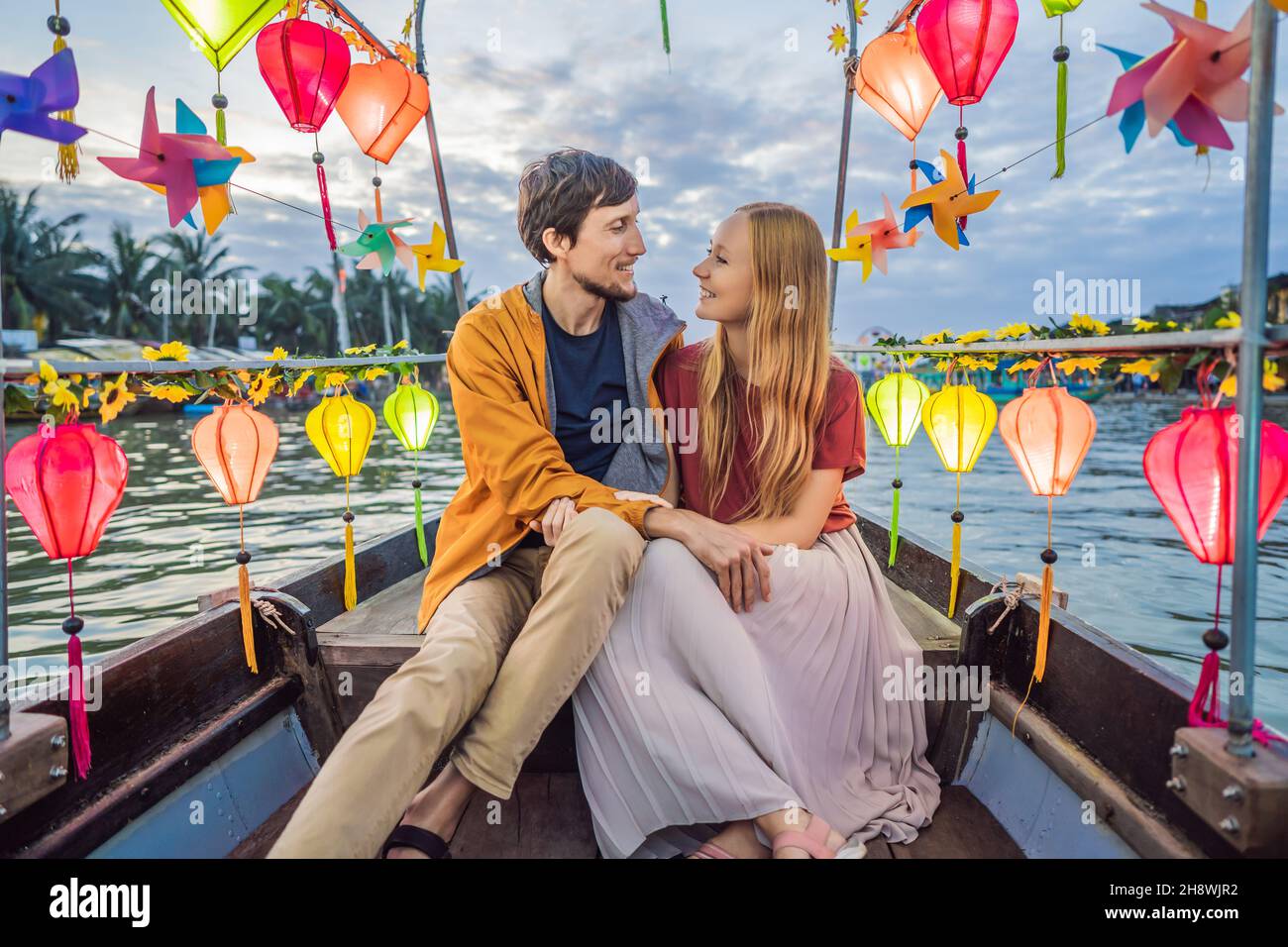 Happy couple of travelers ride a national boat on background of Hoi An ...
