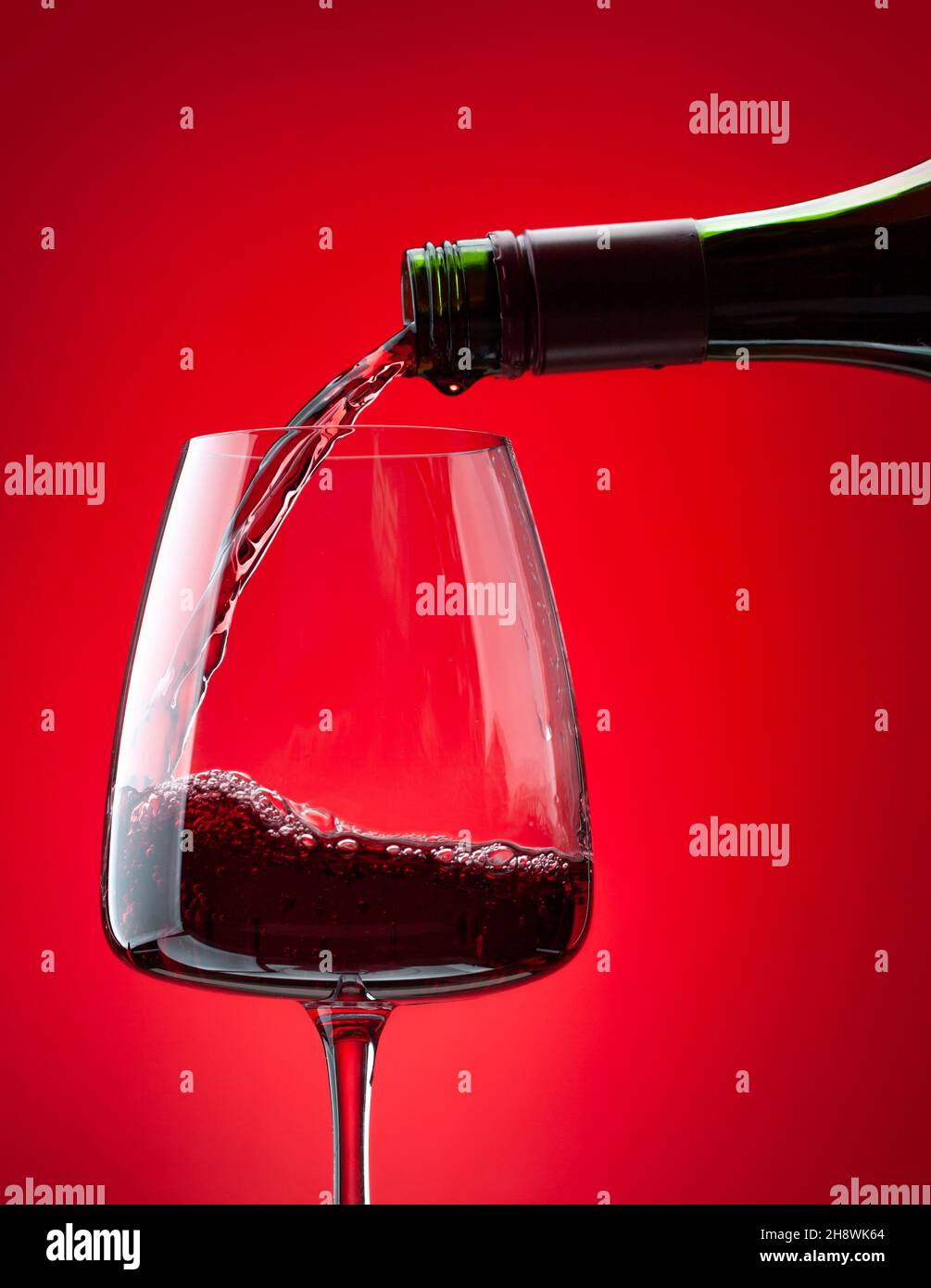 Red wine pouring from bottle into glass over red background Stock Photo