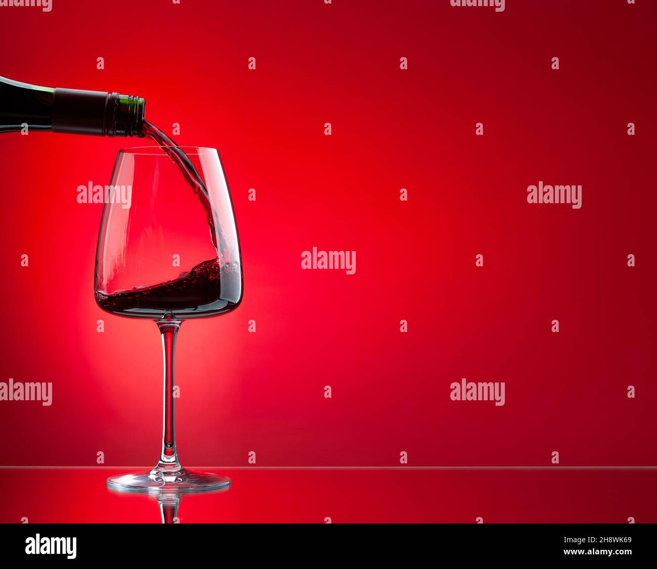 Red wine pouring from bottle into glass over red background Stock Photo