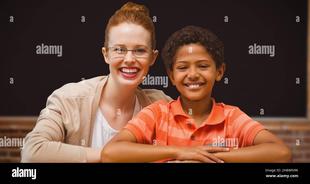 Portrait of smiling redhead teacher sitting with afro student in classroom Stock Photo