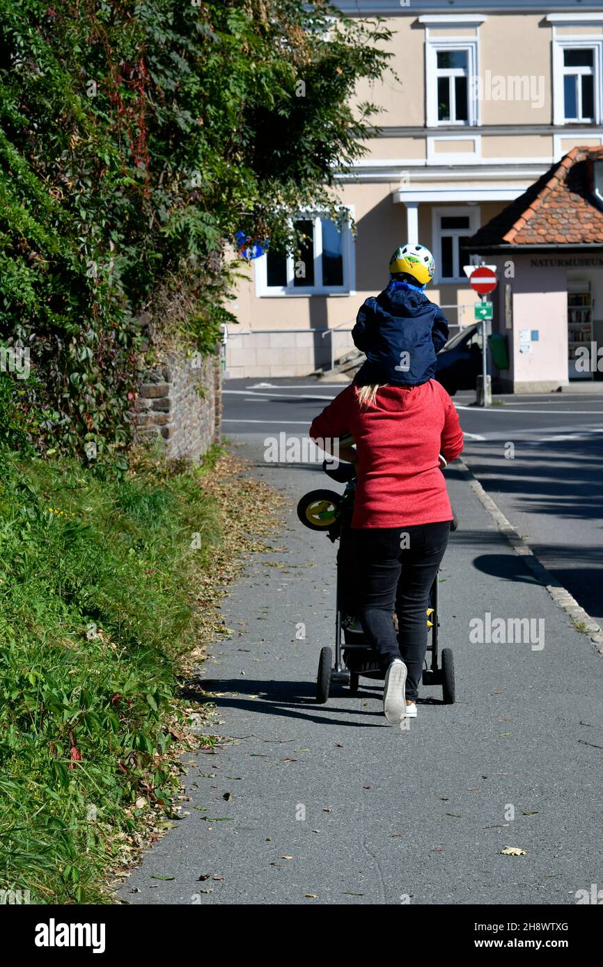 Stainz, Austria - September 23, 2021: Unidentified mother with baby carriage and child piggybacking, another funny kind of transport Stock Photo