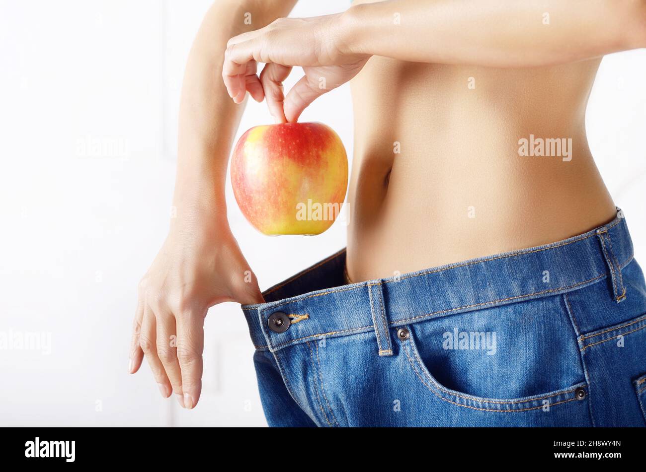 Caucasian female model in blue jeans with red apple showing her flat stomach. Healthy lifestyle and Weightloss concept. Stock Photo