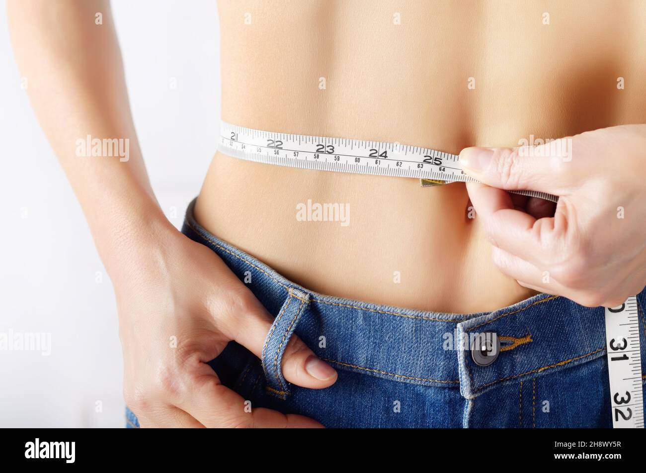 Caucasian female model in blue jeans with tape measure showing her flat stomach. Healthy lifestyle and Weightloss concept. Stock Photo