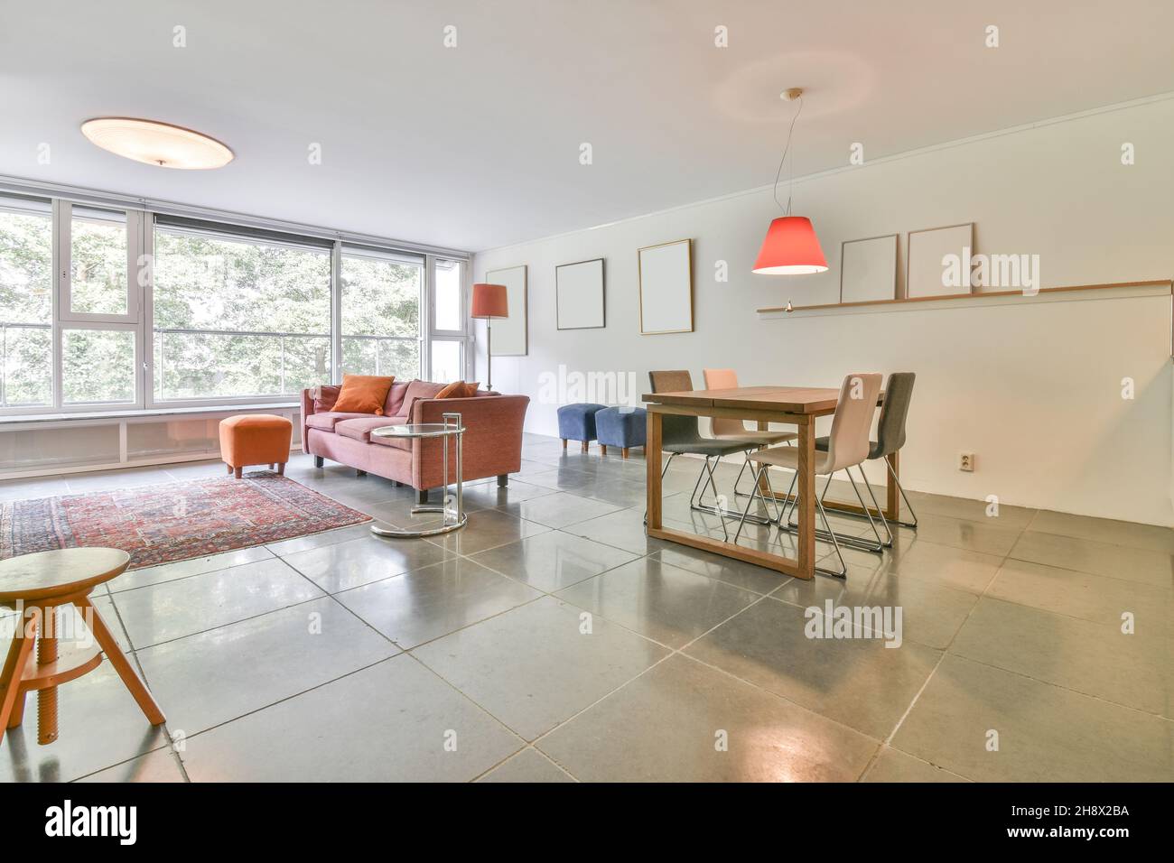 Comfortable sofa with cushions placed on tiled floor near orange pouf in light spacious living room with windows in apartment Stock Photo