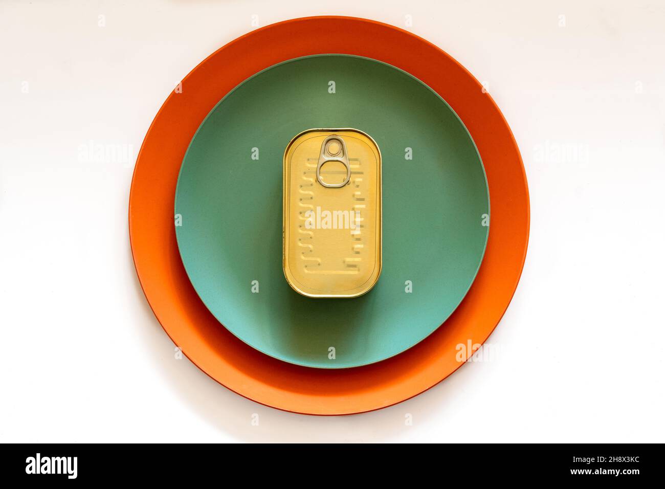 From above of rectangular closed tin can placed on green and orange round plates on white table Stock Photo