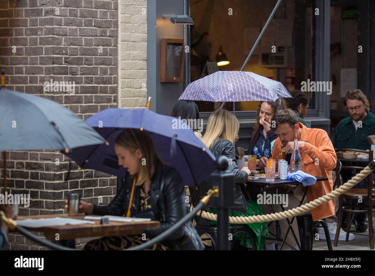 Diners shelter from rain under umbrellas in an outdoor space in London as only outdoor dining is permitted under the current Covid rules. Stock Photo