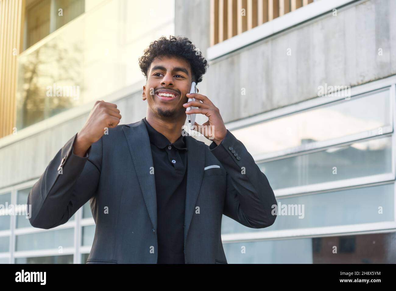 Happy young Indian male with curly dark hair wearing suit walking on street  near modern building and having conversation on mobile phone while looking  Stock Photo - Alamy