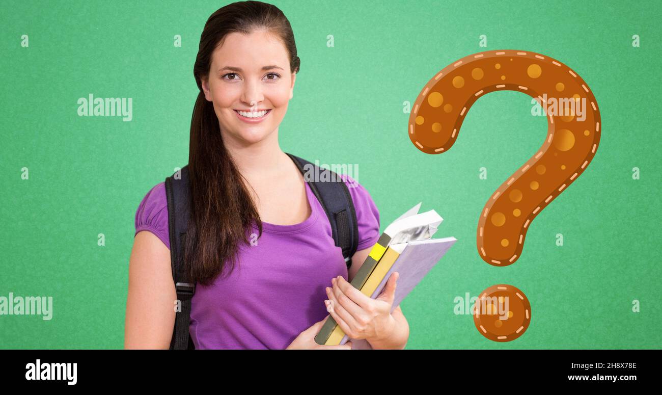 Portrait of smiling young woman holding books by brown question mark over green background Stock Photo