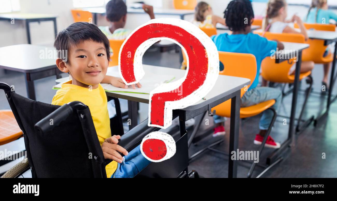Digital composite of red question mark over smiling disabled schoolboy sitting at desk in classroom Stock Photo