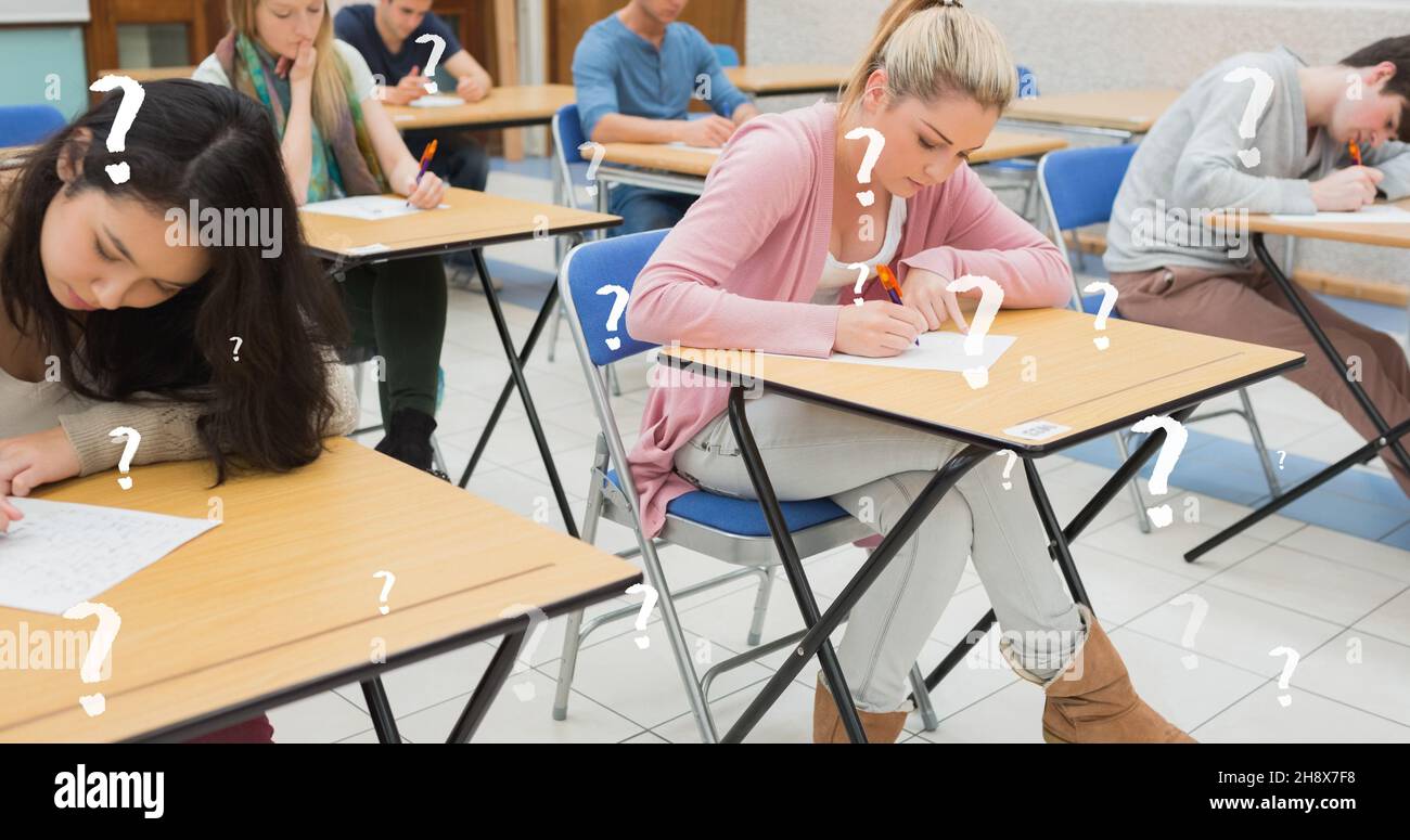 Digital composite image of college students writing exam at desks in classroom with question marks Stock Photo
