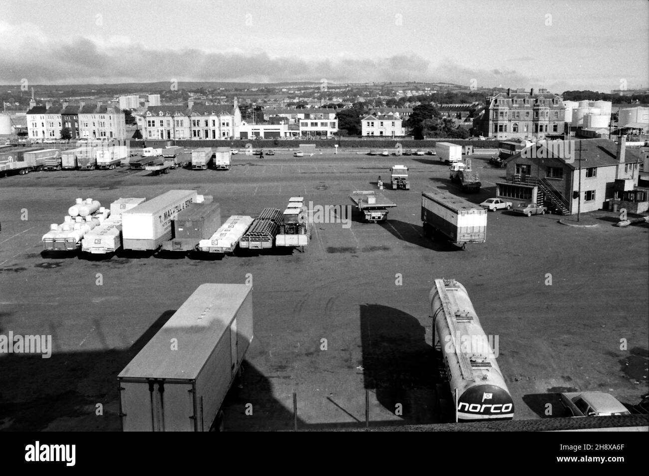 Trailers and containers at the ferry terminal in Larne, Northern Ireland. With houses and H.M. Coastguard building on Olderfleet Road beyond. Taken from P&O Freight Ferry M/V Bison. February 1984 Stock Photo