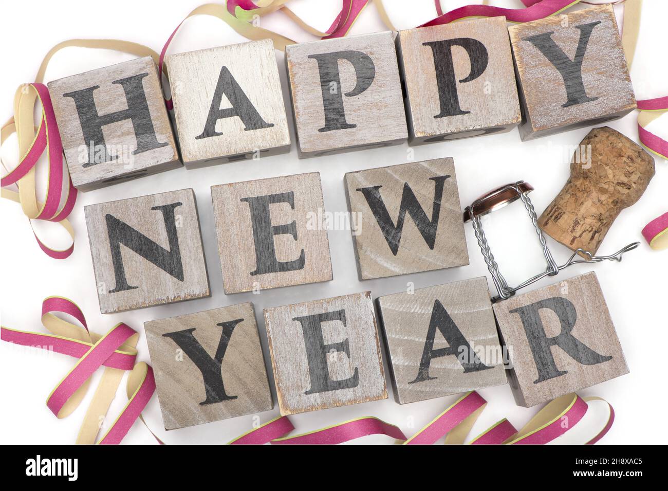 wooden letter cubes representing happy new year framed by party garland and isolated with a champagne cork on white background new year's evening Stock Photo